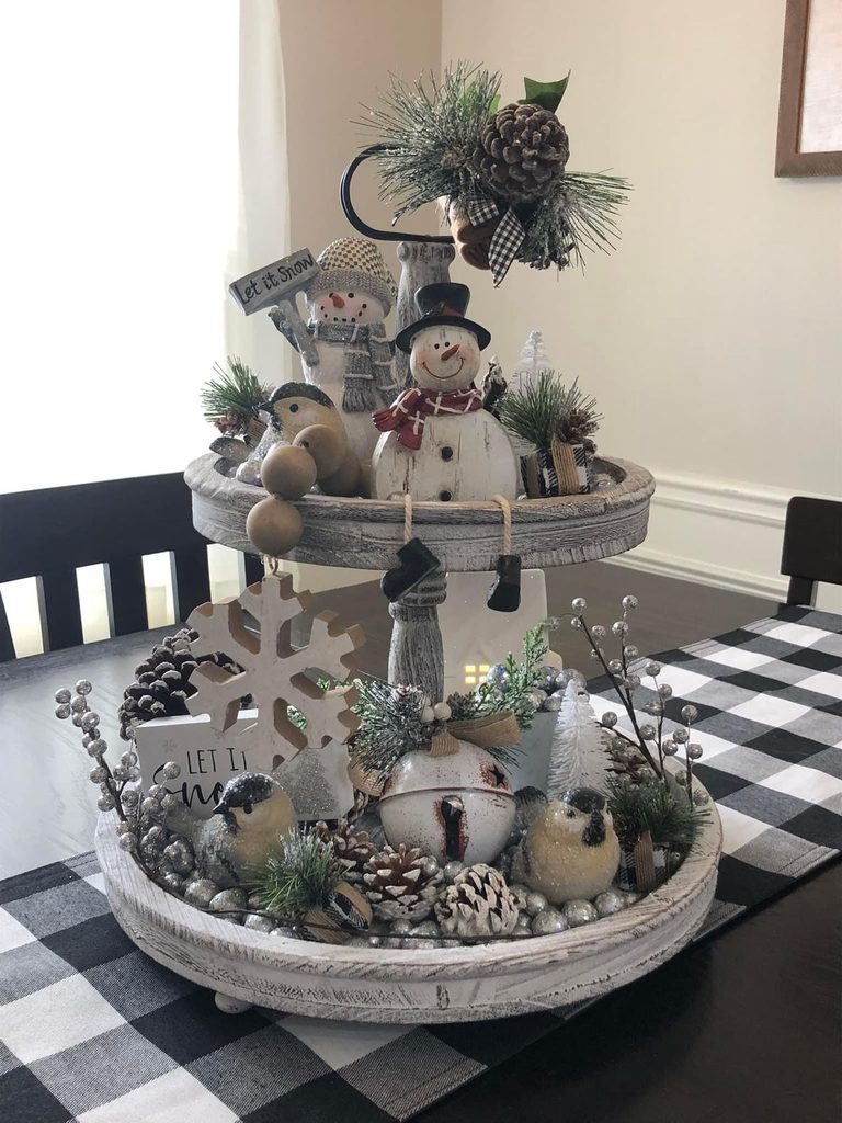 Two-tier white wood tray with snowmen, birds, pinecones and a snowflake on a black and white plaid runner