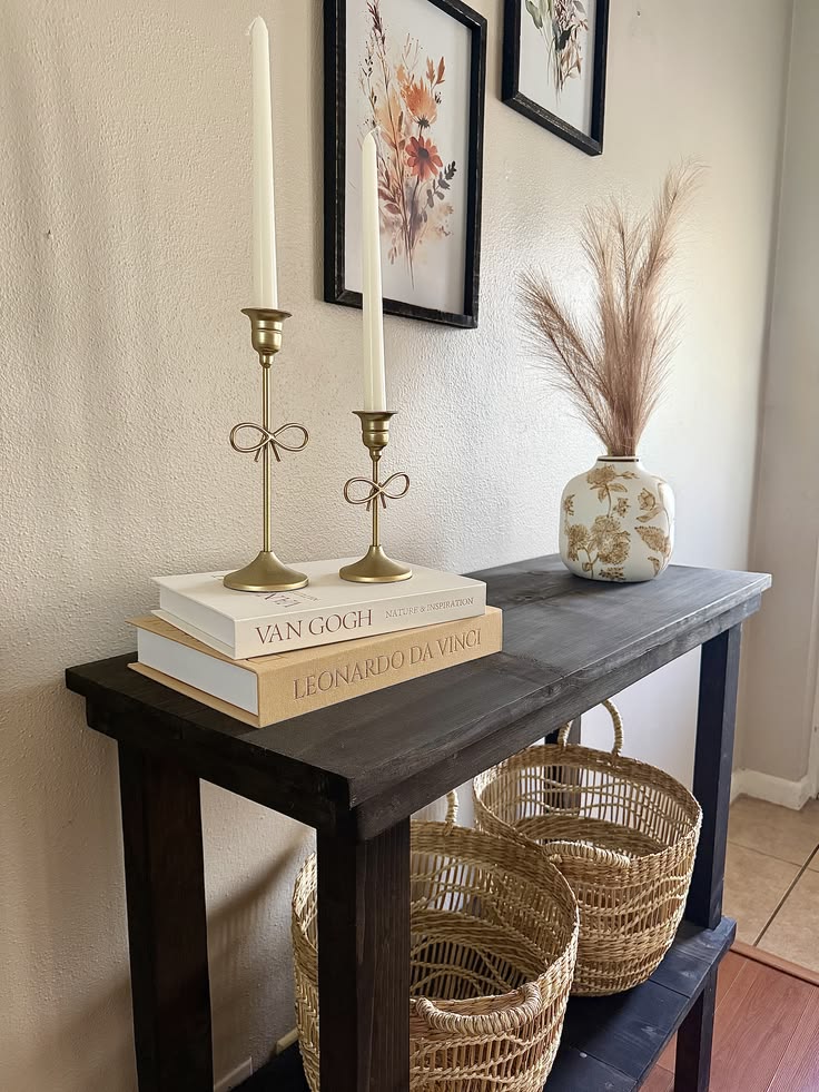 two stacked coffee table books topped with gold candlesticks on a dark wood console table, small entryway table decor