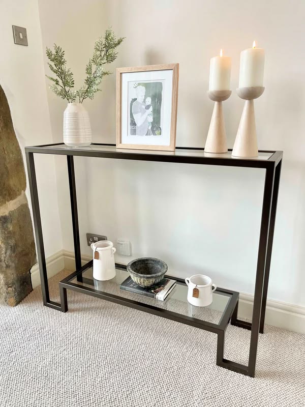slim black metal and glass two-tier console table with a framed print and two candles, small entryway table decor