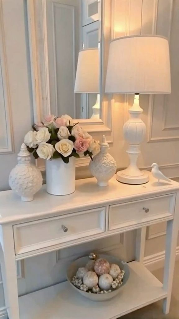white console table with two drawers, a large table lamp and a vase of roses, small entryway table decor